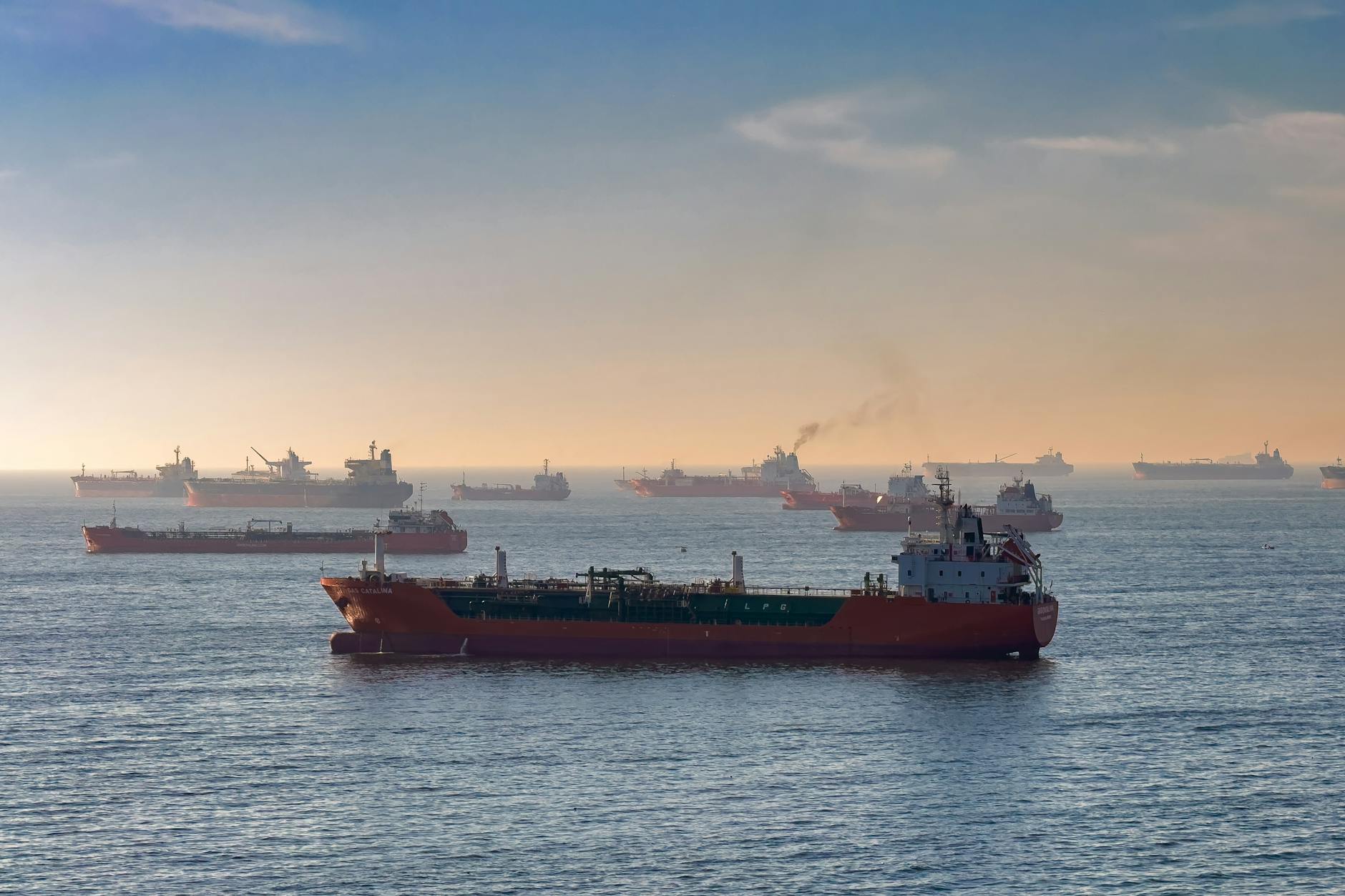 Oil tanker passing through the Strait of Hormuz with naval vessels in the background